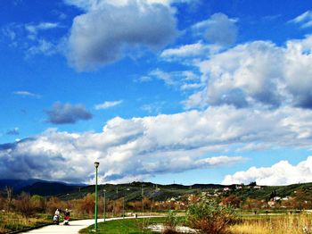 Road passing through field against cloudy sky