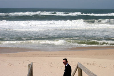 Side view of man wearing sunglasses standing at beach during sunny day