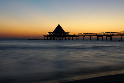 Silhouette built structure on sea against sky during sunset