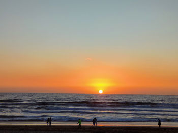 People on beach against sky during sunset