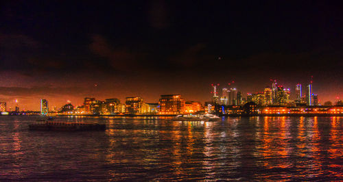 Illuminated buildings by sea against sky at night