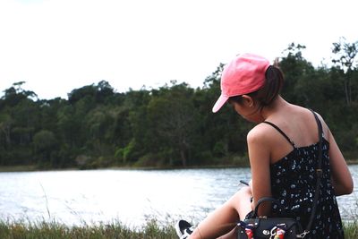 Woman sitting by lake against sky