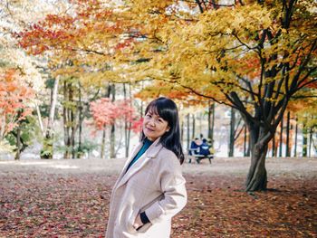 Smiling young woman standing by trees during autumn