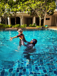 Little girl and her mother swimming together in a swimming pool at a tropical resort