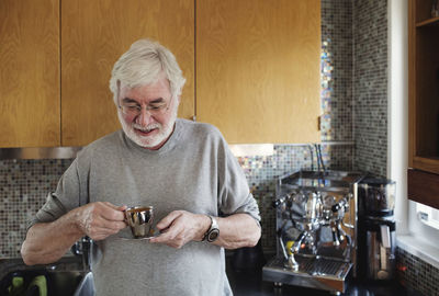 Smiling senior man holding coffee cup while standing at kitchen counter