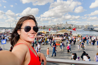 Portrait of woman wearing sunglasses taking selfie while standing by railing