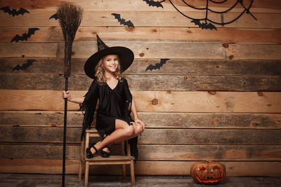 Girl sitting on seat wearing halloween costume against wall