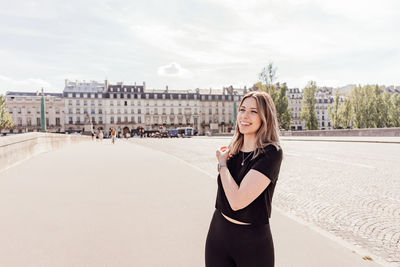 Portrait of smiling young woman standing against sky in city