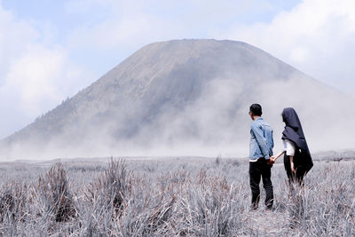 Rear view of men standing on landscape against sky at bromo mountain