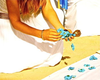 Midsection of woman decorating fabric with blue flowers during wedding ceremony