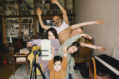 Happy family filming dance with hands raised on smart phone at home