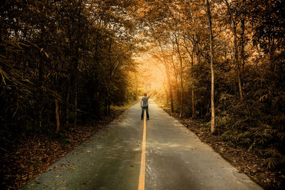 Rear view of man standing on road amidst trees during autumn