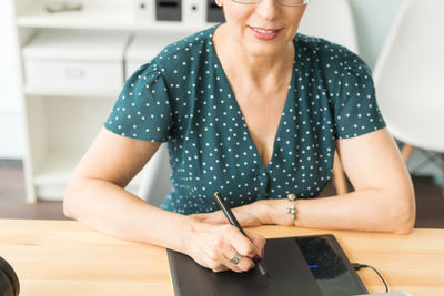 Midsection of woman sitting on table at home