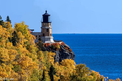 Lighthouse amidst trees and sea against sky
