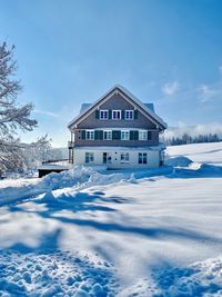 Snow covered house by building against sky