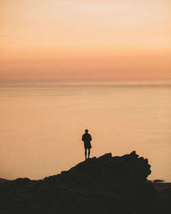 Silhouette man looking at sea against sky during sunset