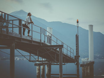 Man standing on railing by bridge against sky