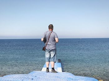 Rear view of man standing in sea against clear sky