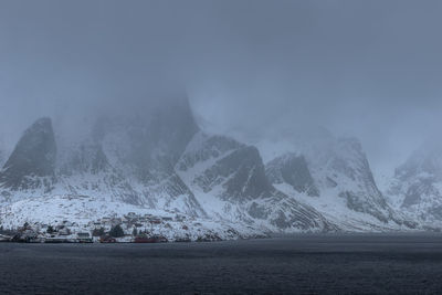 Scenic view of sea by snowcapped mountains against sky