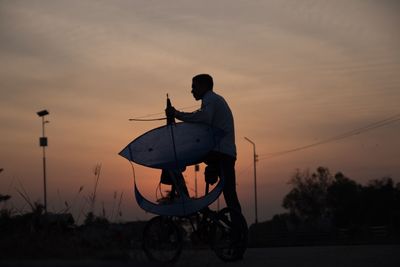 Man standing by silhouette bicycle against sky