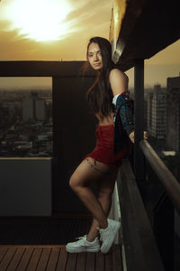 Portrait of young woman standing by railing against sky