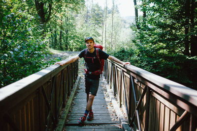 Full length portrait of man standing on footbridge in forest