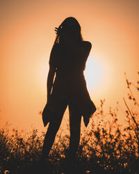 Rear view of silhouette woman standing on field against sky during sunset