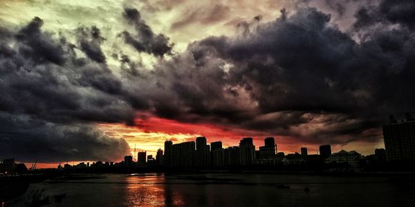 Buildings in city against dramatic sky during sunset