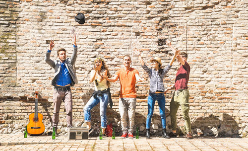 Cheerful friends throwing confetti while standing against brick wall