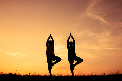 Silhouette people with arms raised on field against sky during sunset