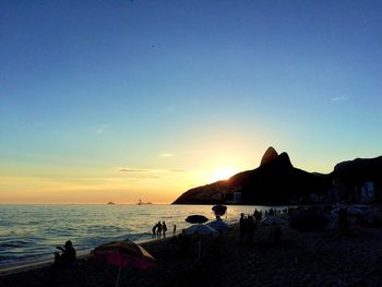 Silhouette people on beach against clear sky during sunset