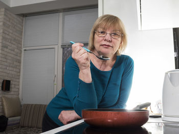 Portrait of mature woman holding spoon in kitchen at home