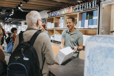 Smiling salesman showing appliance box to customers at checkout counter in electronics store