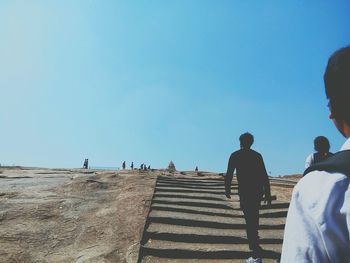 Rear view of people walking on steps against clear blue sky