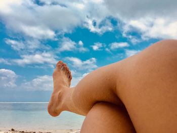 Midsection of man relaxing on beach against sky