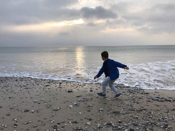 Boy standing on beach against sky during sunset