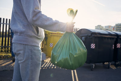 Man walking with rubbish. hand carrying plastic bag against garbage cans on street.