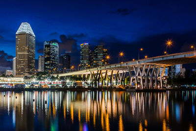 Illuminated modern buildings by river against sky at night