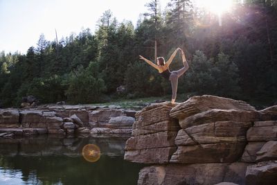 Full length of woman doing yoga on rock against trees