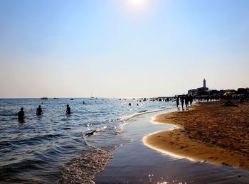 People on beach against clear sky during sunset