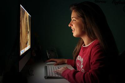 Side view of smiling young woman using computer at home