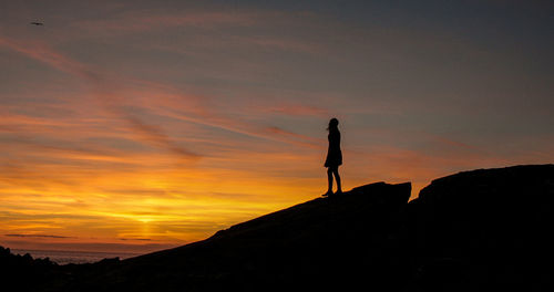 Silhouette woman standing on mountain against orange sky