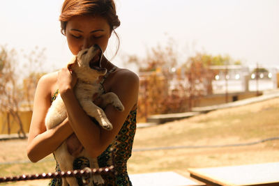 Woman holding dog while standing on footpath