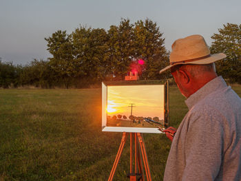 Old man painting sunset in mirror 