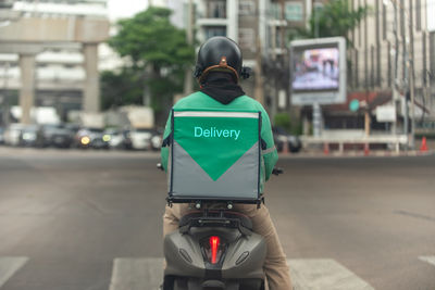 Rear view of man riding motor scooter on street in city