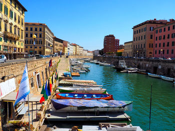 Boats moored in canal amidst buildings in city against clear blue sky