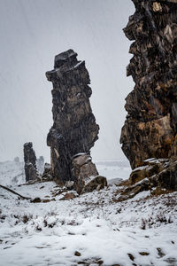 Rock formation on snow field against sky