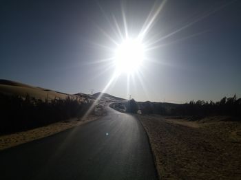 Road passing through landscape against sky on sunny day