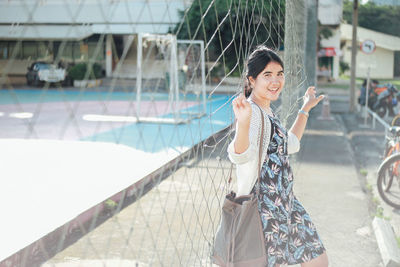 Portrait of young woman leaning on net in court