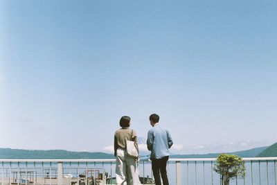 Rear view of friends standing at lakeshore against sea